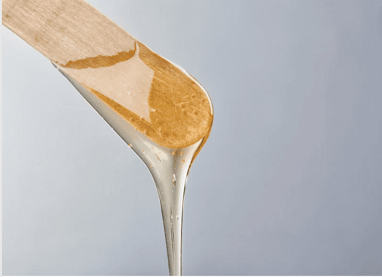 Honey dripping from a wooden dipper against a grey background.