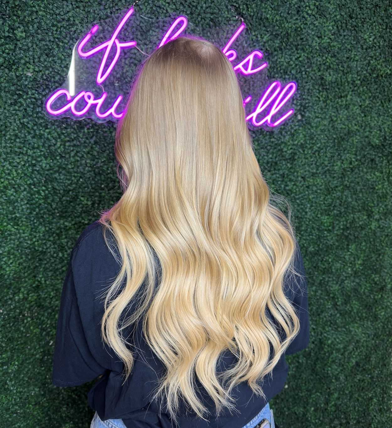 Woman with long blonde wavy hair against a neon sign background.