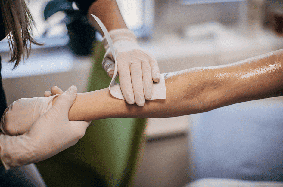A health professional is applying an adhesive bandage to a patient's arm.
