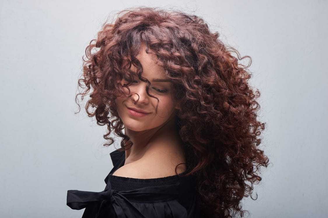 Woman with voluminous curly hair smiling with closed eyes.